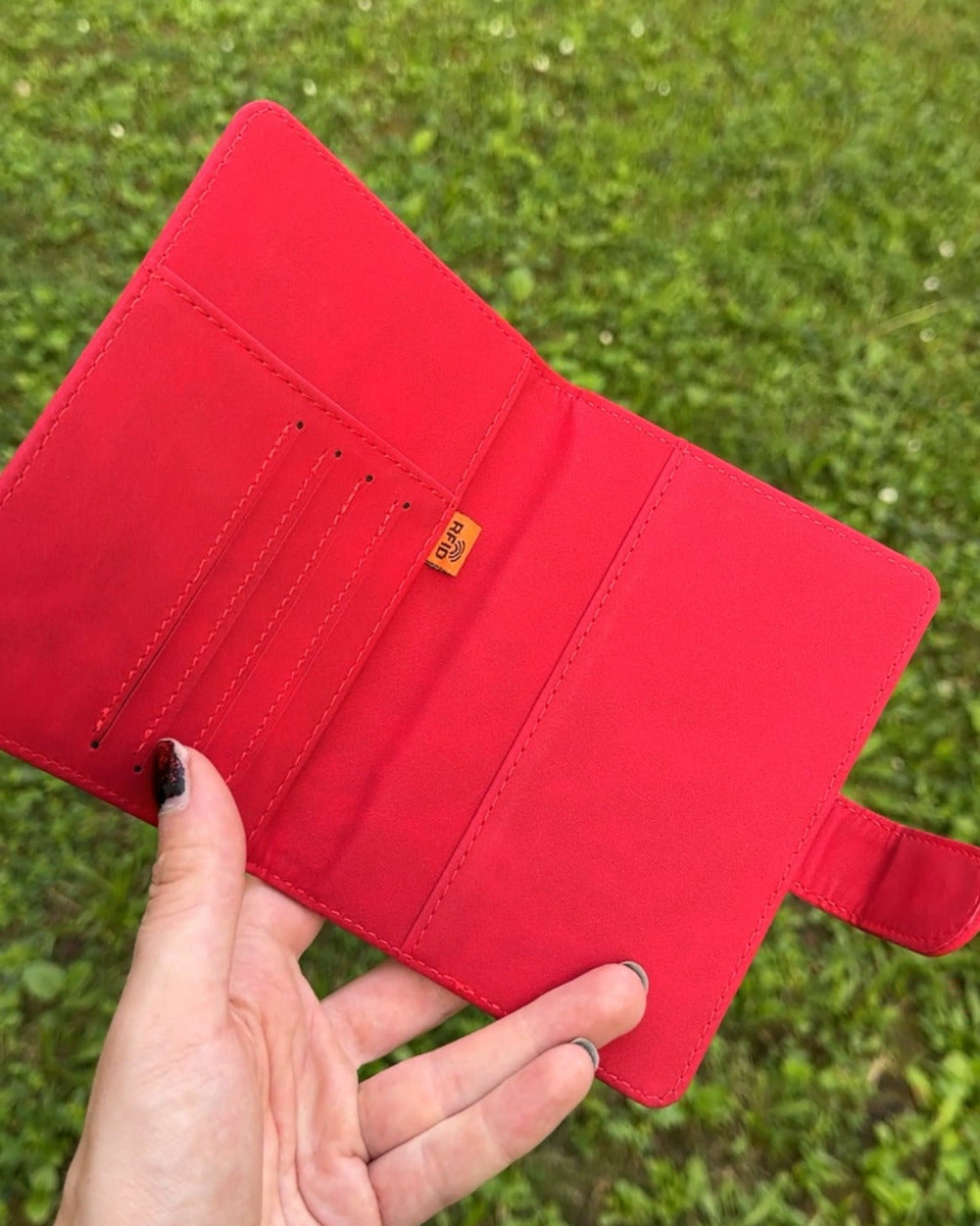 Red passport cover held in a hand against a grassy background